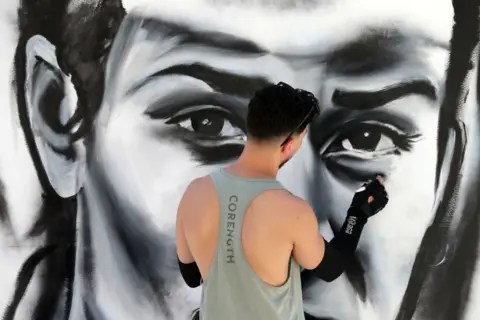 BILLEL BENSALEM / GETTY IMAGES A man paints a mural of Olympic champion boxer Imane Khelif's face.