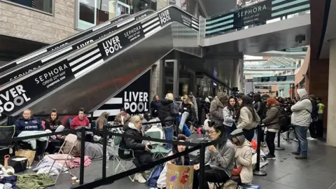 People camp out in the open in Liverpool One outside the new Sephora store. People can be seen say in sleeping bags and stood queuing outside the entrance.