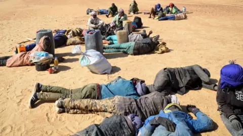 Getty Images This photo from 2019 shows a group of migrant men resting before carrying on their journey across the Air dessert, northern Niger, towards the Libyan border
