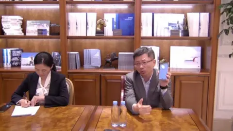 Mr Jiang, right, holds up a phone to the camera during an interview