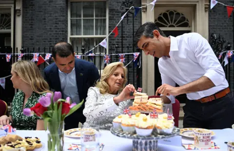 EPA British Prime Minister Rishi Sunak (R) offers US First Lady Jill Biden a sandwich during a coronation big lunch for community heroes, Ukraine refugees, and youth groups at 10 Downing Street in London, Britain, 07 May 2023, following the coronation of Britain's King Charles III at Westminster Abbey in London on 06 May.