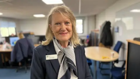 Kate Bradbrook/BBC Lynn Hinch, pictured with long light-coloured hair, wearing a striped scarf in an office