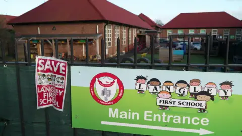 A general view of the entrance to Langley First School. On the railings outside there is a large banner pointing to the school's entrance and a poster saying Save Langley First School.