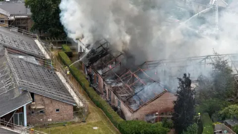 Ian/Yorkshire Visions Media Smoke billows from the roof a large building while the fire service dampens flames with a hose.