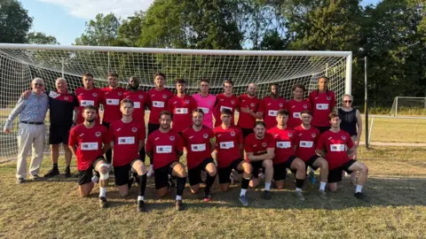 Clive Seeley A photo of a football team standing in front of a net, half the team are kneeling down they are all wearing red shirts 