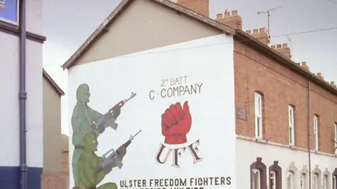 Pacemaker A mural on the gable wall of a terrae house on Belfast shows two masked gunmen in green combat clothes, one of whom is standing and the other kneeling, both carrying automatic rifles. The mural says 2nd battalion, C Company, Ulster Freedom Fighters