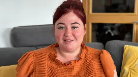 Naomi Allsop sat on a sofa wearing an orange top