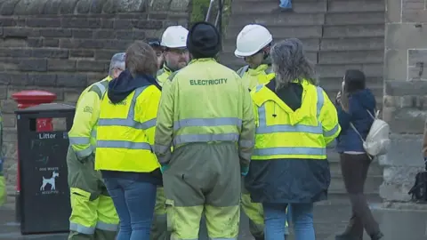 A huddle of engineers stand in the street wearing high vis jackets.