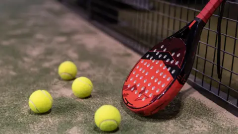 A padel and four yellow balls