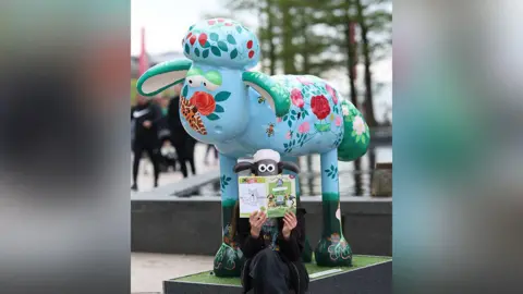 Liverpool ONE A person holding a Shaun the Sheep map with a Shaun the Sheep mask sits at one of the nine Shaun the Sheep markers in a special trail at Liverpool ONE.