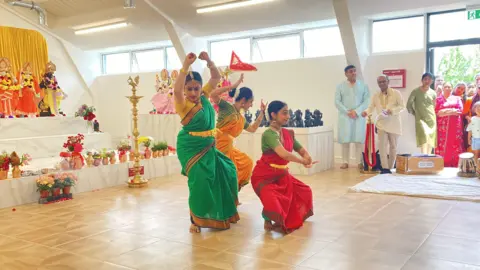 Hindu dancers perform in colourful saris in front of a stage full of religious statues