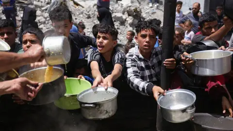 Displaced Palestinians gather to collect portions of cooked food at a charity distribution point in Jabalia in the northern Gaza Strip on May 19, 2025