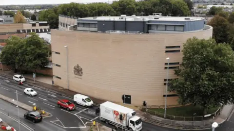 Jonny Michel/BBC An aerial shot of Cambridge Crown Court on a dreary day, with its curved walls and a large tree the focus of the image. Traffic queues parallel to the court.