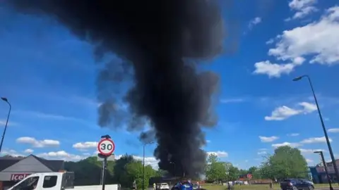 Paul Yates Huge dark plume streams upwards aginst the blue sky with roads in front of the affected site