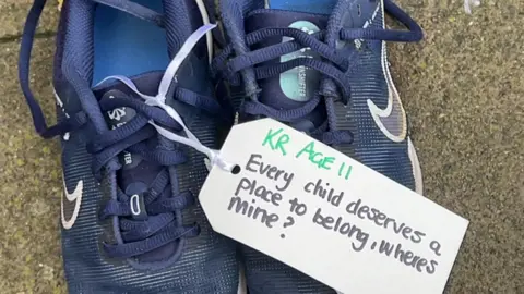 A pair of blue trainers with a label attached, saying 'Every deserves a place to belong, where's mind?' 