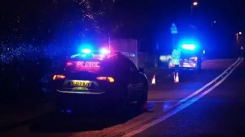 Eddie Mitchell Two police cars at the side of the road with their blue lights on