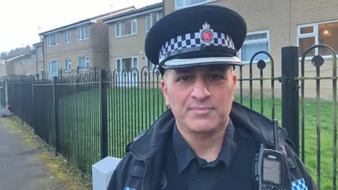 Photograph of Chief Superintendent Shan Nasim from Greater Manchester Police. He is pictured in front of flats on the Hart Mill Estate in Mossley. 