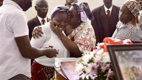 The mother of Antonio Juaqim weeps by his coffin, while another woman puts her arms around her to console her