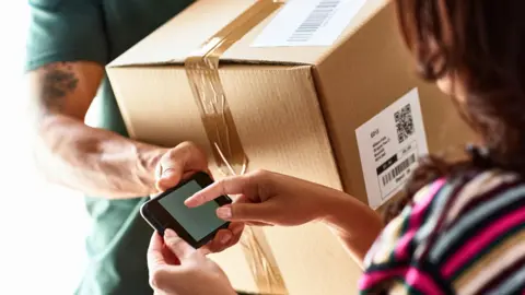 Getty Images Cropped image of woman receiving delivery at front door - it's a brown parcel from a courier