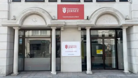 BBC Front view of Government of Jersey building with name sign between two sets of twp columns with arched detailing on the front of the building and glass doors leading inside