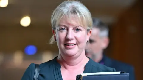 Getty Images Shona Robison, wearing a blue top, carrying a folder and looking at the camera in the Scottish Parliament 