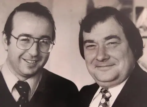 Bob Downing A black and white image of Rob Bishop standing next to Bob Downing. Rob is wearing glasses and they both have light-coloured shirts and ties on. 