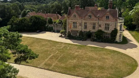 National Trust Outlines can be seen on an oval shaped lawn in front of a large stately home.