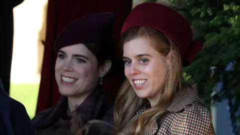 Reuters Britain's Princess Beatrice and Princess Eugenie smile. They are wearing hats and coats