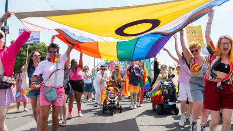 Pride parade walking holding flags wearing bridge / rainbow coloured outfits.
