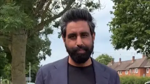 Jeevun Sandher has greying hair and is wearing a suit. 