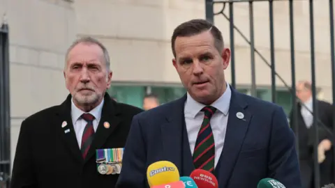 PA Media A man with short dark hair is speaking into a number of coloured microphones