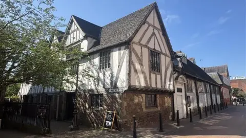 A timber-framed building on a pedestrianised street bathed in spring sunshine