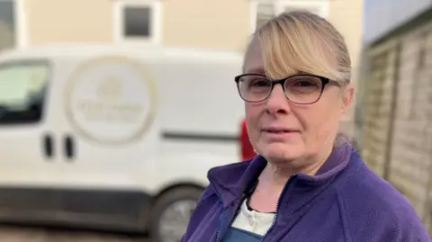 Alison Kennedy of Ffos Farm stands in front of her white delivery van.  She has blonde hair, black rimmed glasses and is wearing a purple fleece.