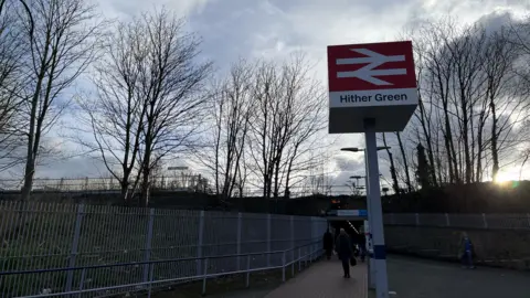 The sign outside Hither Green station with the station in the background. 