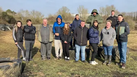 Together Connect NN A group of people standing in a field near large industrial tyres