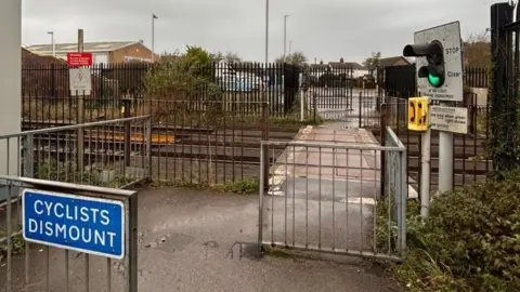 Staggered metal fencing with traffic light for pedestrians at entrance on to pedestrian level crossing