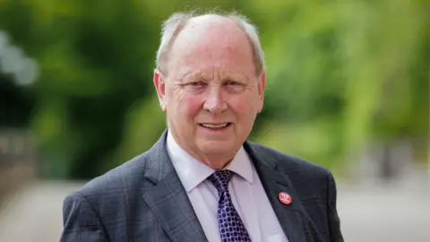 PA Media Jim Allister wearing a suit and tie, looking at the camera with a slight smile.