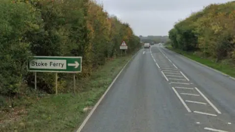 Google The A134 in Stoke Ferry. It is a single carriageway road and there is a green road sign on the left of the picture which says Stoke Ferry and is directing people to it on the right.