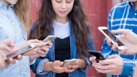 Group of teenagers standing together looking at their phones 