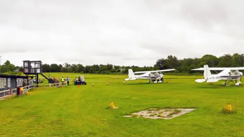 Popham, near Basingstoke, England - August 2021: Small light aircraft parked in front of the buildings and control tower of Popham airfield. 