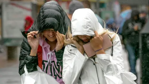 Two women pull their hoods down as they walk down a street in the rain
