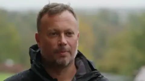 Wildwood Trust Mark Habben wears a black raincoat as he looks into the distance
