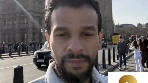 Iqbal and Sons Bereavement Services Ali Alshmari in a selfie. We can see he is in London and Big Ben his behind him. There are tourists in the background. He is an Asian man. He has a beard and short black hair. 
