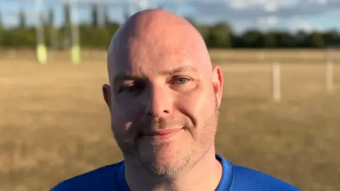 Matthew Pearson smiles straight at the camera while standing on a rugby pitch.