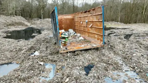 BBC / Ben Leete A woodland scene with piles of waste and a skip in the forefront