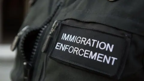 A close-up shot of the badge of an Immigration Enforcement officer, photographed during a raid a residential property looking for illegal immigrants in London  