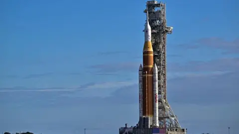 An image of a mega rocket in a stable position, surrounded by blue skies, before it was rolled towards the Kennedy Space Center in Cape Canaveral, Florida.