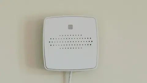 Ally Cares The sensors are hidden within a white square plastic box attached to a wall. It detects any change in a resident's breathing or movement at night and sends an alert to care staff if it picks up anything unusual.