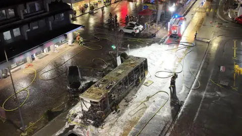 Fribourg Police/EPA/Shutterstock View from above the incident showing burnt out bus surrounded by foam and fire hoses in central area of town.