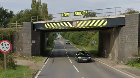 A railway bridge over a road.  It has a sign saying low bridge on it